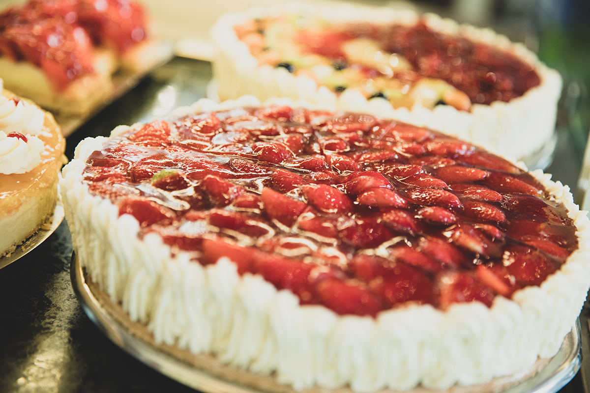 Das Bild zeigt eine Erdbeertorte mit weiteren Torten im Hintergrund