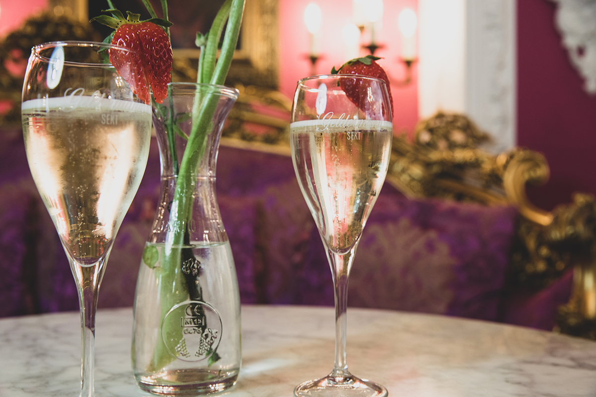 2 Sektgläser und eine kleine Karaffe mit Blumen darin stehen auf einem Tisch