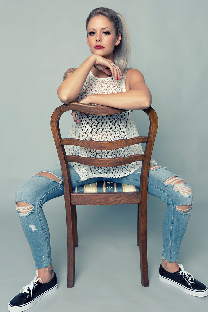 Blonde Frau sitzt  verkehrt herum auf einem Stuhl und lehnt ihre Arme auf die Rückenlehne.